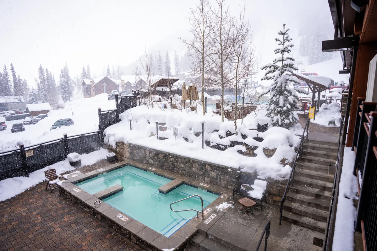 A serene exterior view of a hot tub set against a snow-covered landscape, with trees and mountain views in the background. It evokes relaxation and a sense of luxury after a day of activities.