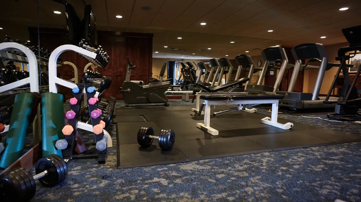 An inviting interior shot of the on-site fitness room, equipped with free weights, treadmills, and benches. The clean, motivating space offers opportunities for both focused solo workouts and group fitness, supporting the narrative of self-care and wellness.