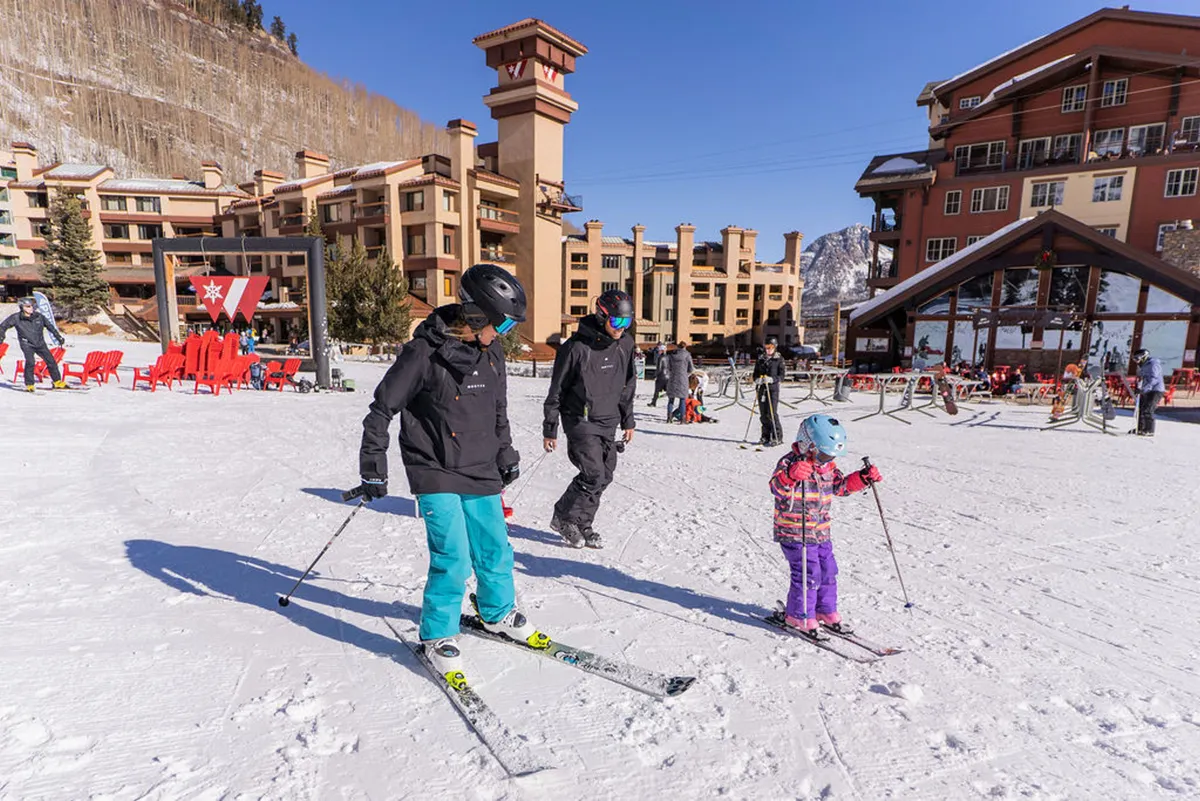 This exterior image captures the lively atmosphere outside the property, with skiers of various ages preparing for a day on the slopes. The snow-covered ground and welcoming building façade highlight resort-style living and direct access to skiing and winter sports. Visible ski equipment and bundled-up families convey the excitement and accessibility of outdoor adventure right at the doorstep.