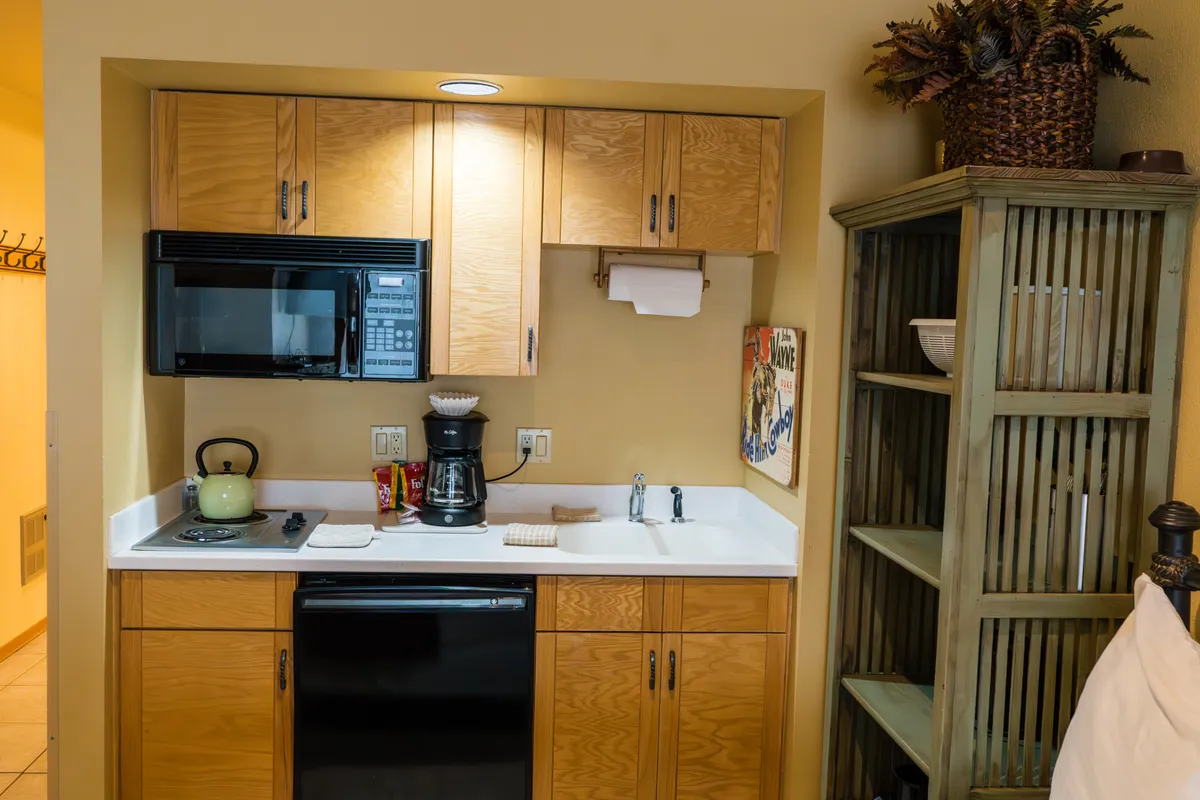 A close-up of the kitchen area, focusing on kitchen appliances such as a coffee maker, toaster, and microwave, with wooden cabinets and a shelf holding decorative items. The cozy ambiance highlights the convenience and warmth of the space for meal preparation and casual dining.