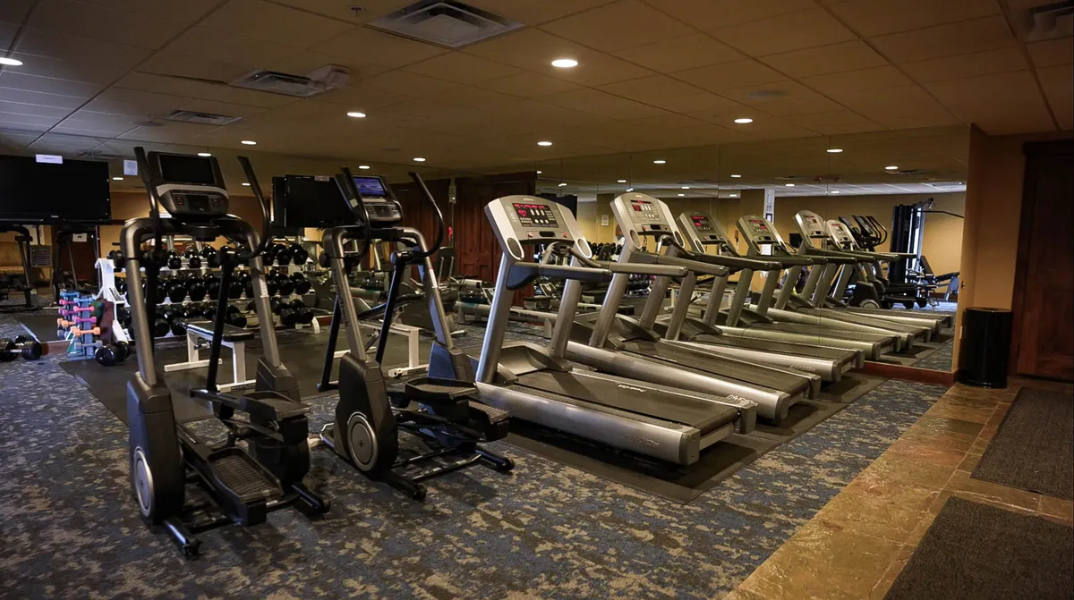 An inviting interior image of a modern fitness room equipped with treadmills, ellipticals, and free weights. The space is bright and energetic, encouraging an active lifestyle.