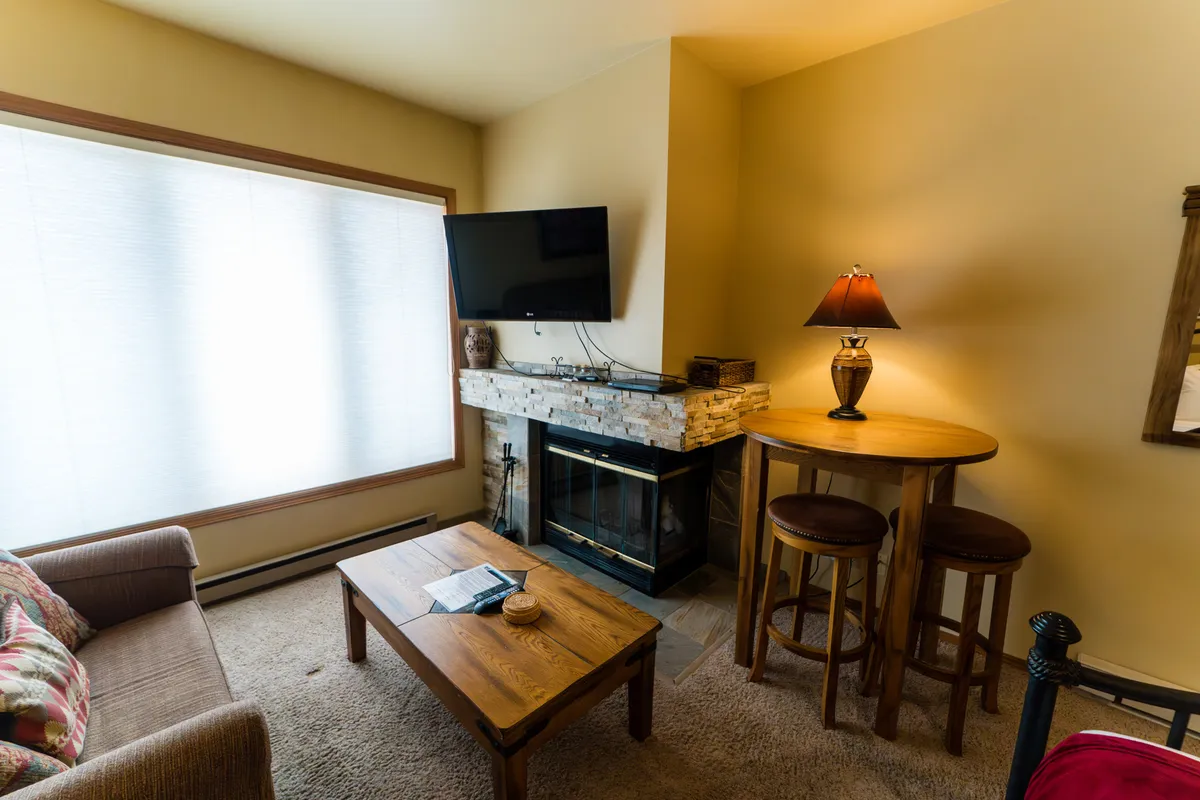 A view of the studio’s sitting area featuring a comfortable sofa and bar table, with a glowing fireplace as the focal point. The space exudes warmth and invites both relaxation and socializing, with soft lighting enhancing the cozy atmosphere.
