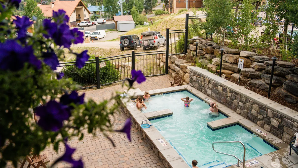 This exterior image highlights a resort-style swimming pool and hot tub framed by flowering plants and a welcoming stone wall. The inviting scene suggests opportunities for both relaxation and socializing in a communal outdoor setting.